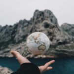 A hand holding a floating globe with a scenic Marseille backdrop, capturing adventure and exploration.