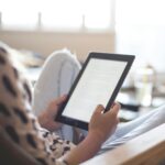 A woman enjoys reading on a tablet, sitting comfortably in a modern living room.