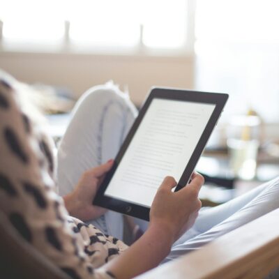 A woman enjoys reading on a tablet, sitting comfortably in a modern living room.