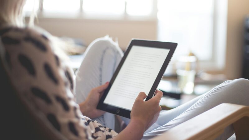 A woman enjoys reading on a tablet, sitting comfortably in a modern living room.