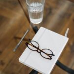A stylish and minimalistic top view of a workspace with glasses, a notebook, and a glass of water on a wooden table.