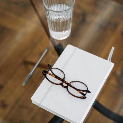A stylish and minimalistic top view of a workspace with glasses, a notebook, and a glass of water on a wooden table.
