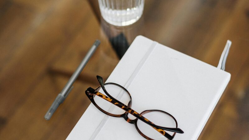A stylish and minimalistic top view of a workspace with glasses, a notebook, and a glass of water on a wooden table.