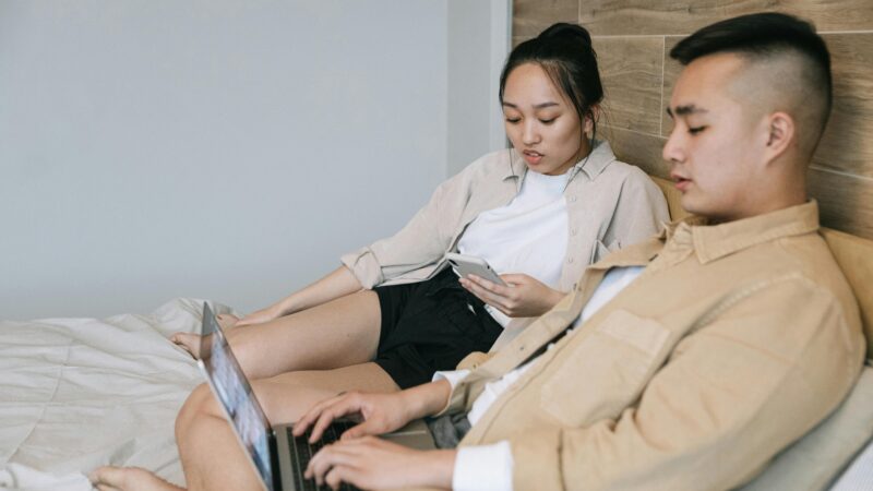 A couple using devices on a bed, enjoying technology in a relaxed indoor setting.